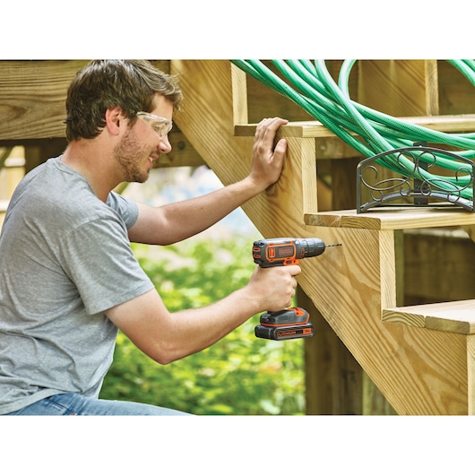 Photo de la perceuse sans fil BLACKDECKER BDCDC18KB utilisée sur des escaliers en bois en extérieur.