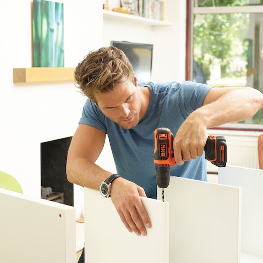 Photo de la perceuse sans fil BLACKDECKER BDCDD12B utilisée pour assembler un panneau de meuble blanc en intérieur.