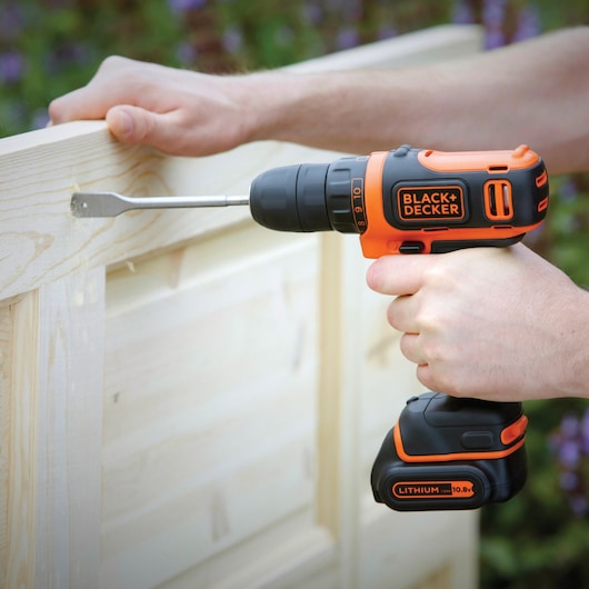 BLACKDECKER BDCDD12B perceuse sans fil utilisée pour percer du bois clair à l’extérieur, design orange et noir.