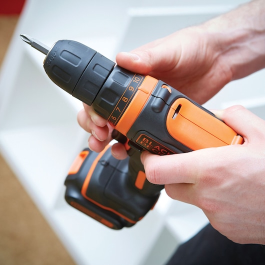 Perceuse sans fil BLACK+DECKER BDCDD12B noire et orange tenue en main, vue rapprochée.