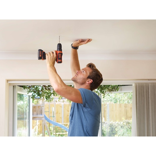Photo de la perceuse sans fil BLACKDECKER BDCDD12 utilisée pour percer un plafond à l'intérieur.