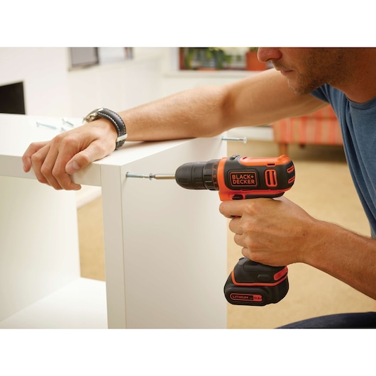 Photo de la perceuse sans fil BLACKDECKER BDCDD12 utilisée pour assembler des meubles blancs en intérieur.