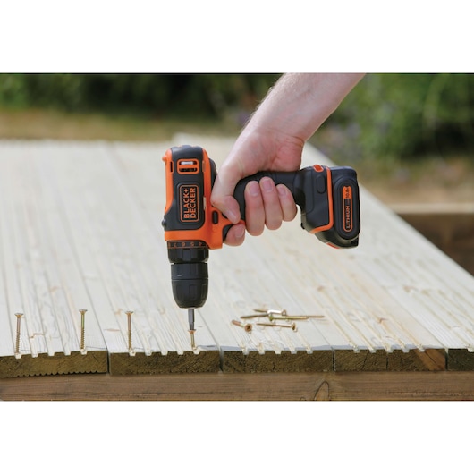 BLACKDECKER BDCDD12 perceuse sans fil utilisée sur du bois avec des vis, photographie extérieure en gros plan.
