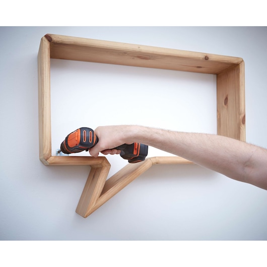 Photo d'une perceuse sans fil BLACKDECKER BDCDD12 utilisée pour fixer une étagère bulle en bois au mur.