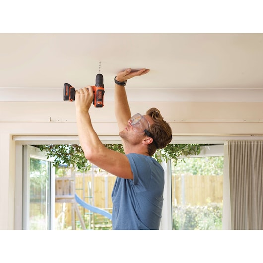 Photo de la perceuse sans fil BLACK+DECKER BDCDD12 utilisée pour percer un plafond en intérieur.