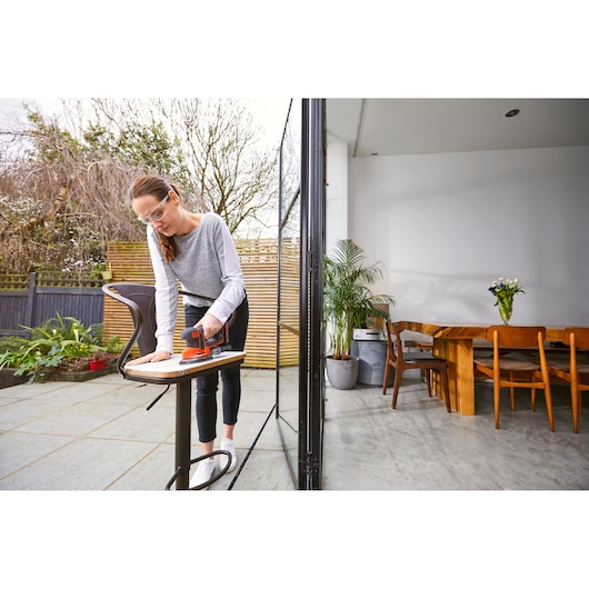 Foto van BLACKDECKER BDCDS18N schuurmachine in gebruik op een houten oppervlak naast een moderne terrastafel.