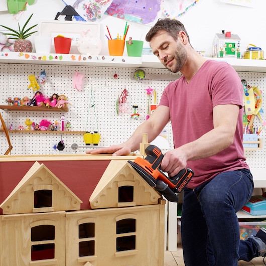 Foto van BLACKDECKER BDCDS18N schuurmachine gebruikt op houten poppenhuisdak in een knutselkamer.