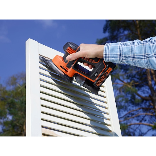 BLACKDECKER BDCDS18 ponceuse sans fil utilisée sur un volet blanc dehors, outil orange et noir tenu à la main.