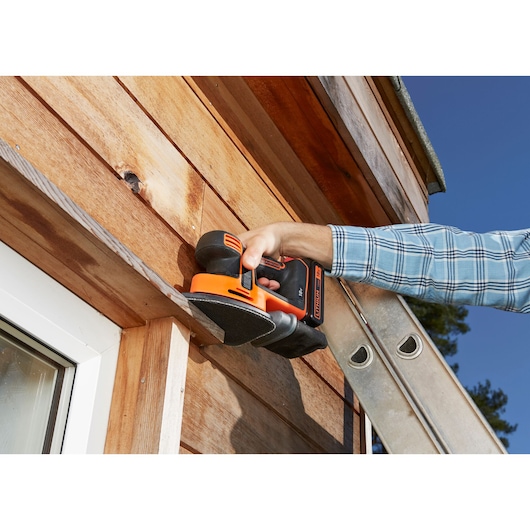 BLACKDECKER BDCDS18 ponceuse sans fil utilisée sur bardage extérieur en bois, scène en gros plan.