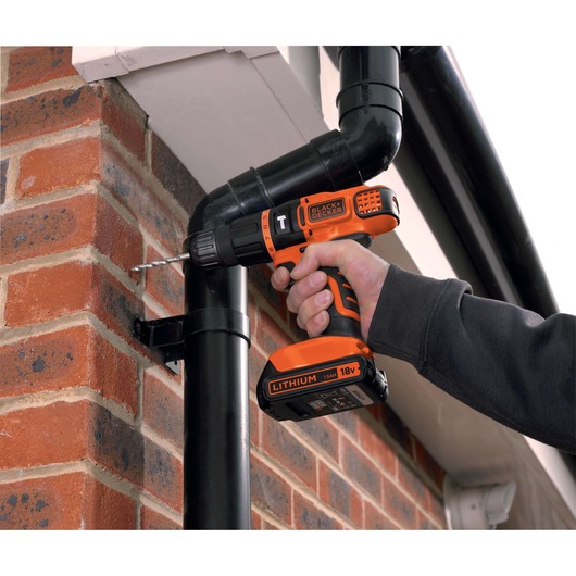 BLACKDECKER BDCH188N perceuse sans fil utilisée pour percer un mur en briques près d'un tuyau noir, vue rapprochée.