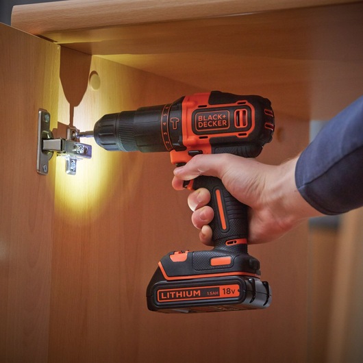 BLACKDECKER BDCHD18KB perceuse sans fil utilisée pour installer une charnière de meuble, batterie lithium 18V visible.