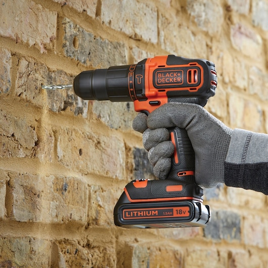 Photo de la perceuse sans fil BLACK+DECKER BDCHD18KB utilisée pour percer un mur de briques, tenue avec un gant.