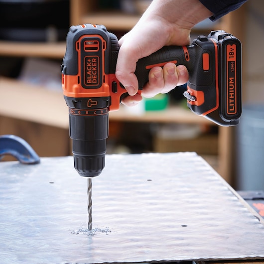 BLACKDECKER BDCHD18K perceuse sans fil orange et noire en action, perçant une plaque métallique.