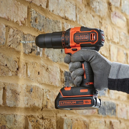 Perceuse sans fil BLACKDECKER BDCHD18K percant un mur en brique, orange et noir, batterie lithium 18V.