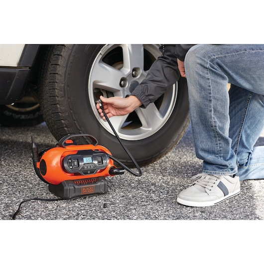 BLACKDECKER BDCINF18N oranje draagbare inflator gebruikt om een autoband buiten op te pompen.