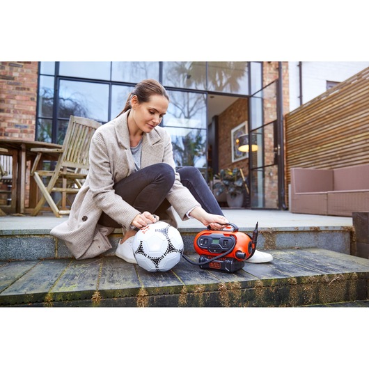BLACKDECKER BDCINF18N oranje draagbare pomp die een witte voetbal buiten opblaast.