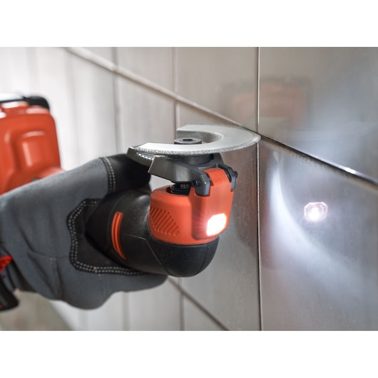 BLACKDECKER BDCOS18N oscillerend multitool in gebruik voor het snijden van tegelspecie, close-up, LED-lampje aan.