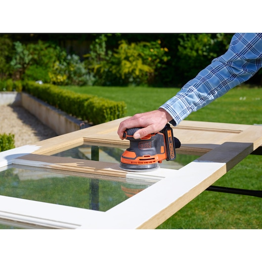 BLACKDECKER BDCROS18N draadloze oranje excenterschuurmachine gebruikt op houten raamkozijn buiten.
