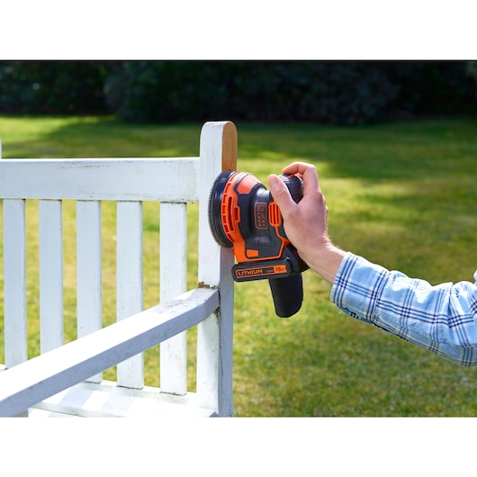 BLACKDECKER BDCROS18N snoerloze excentrische schuurmachine wordt gebruikt om een witte houten stoel buiten te schuren.
