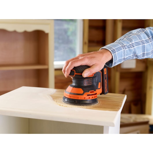 BLACKDECKER BDCROS18 ponceuse orbitale sans fil ponçant une surface en bois dans un atelier.