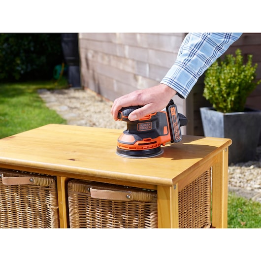 BLACKDECKER BDCROS18 ponceuse orbitale sans fil ponçant une armoire en bois à l'extérieur.