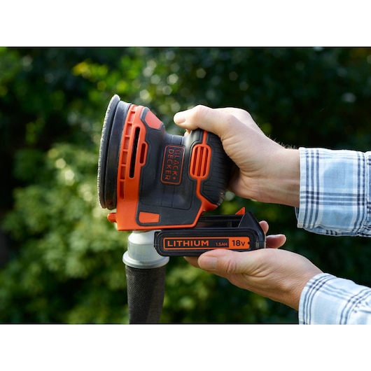 Photo de la ponceuse excentrique sans fil 18V BLACKDECKER BDCROS18 tenue à la main en extérieur.