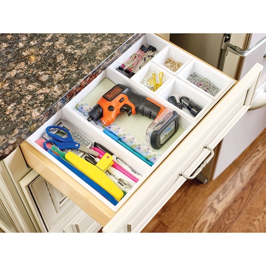 BLACK+DECKER BDCSFS30C tournevis sans fil orange et noir rangé dans un tiroir de cuisine avec des fournitures de bureau, vue de dessus.