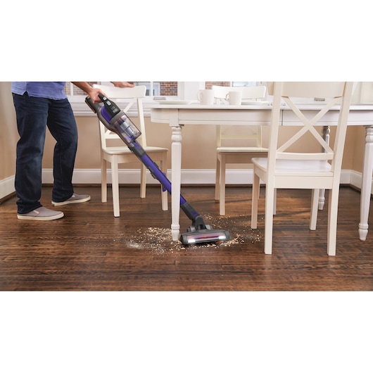 Foto van BLACKDECKER BDPSE1815P snoerloze steelstofzuiger die vuil bij een eettafel op houten vloer schoonmaakt.