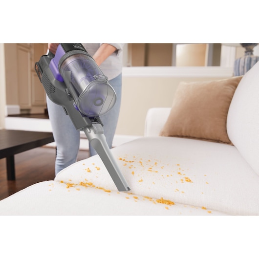 BLACKDECKER BDPSE1815P draadloze stofzuiger verwijdert kruimels van een witte bank in de woonkamer, zijaanzicht.