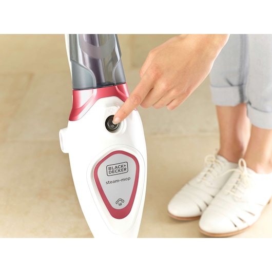 Photo de la BLACK+DECKER BDS1616R balai vapeur activé sur sol beige par une main, motif rouge et blanc.