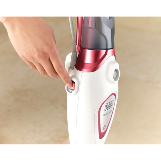 BLACKDECKER BDS1616R balai vapeur en gros plan, main appuyant sur le bouton d'alimentation rouge.