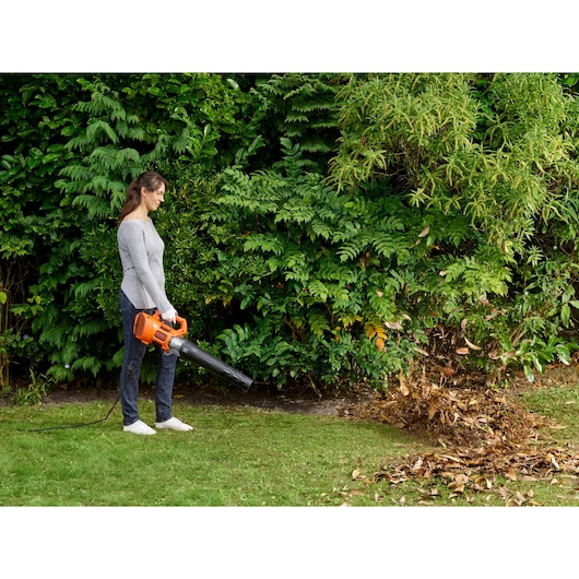 BLACKDECKER BEBL185 bedrade bladblazer in gebruik buiten, oranje en zwart, verwijdert bladeren van het gazon.