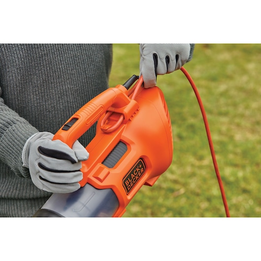 Foto van de oranje BLACKDECKER BEBL185 handbladblazer met snoer, vastgehouden door gehandschoende handen buiten.
