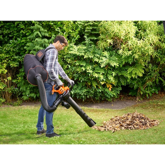 BLACKDECKER BEBLV300 bladblazer met opvangzak in gebruik in een tuin om droge bladeren te verzamelen.