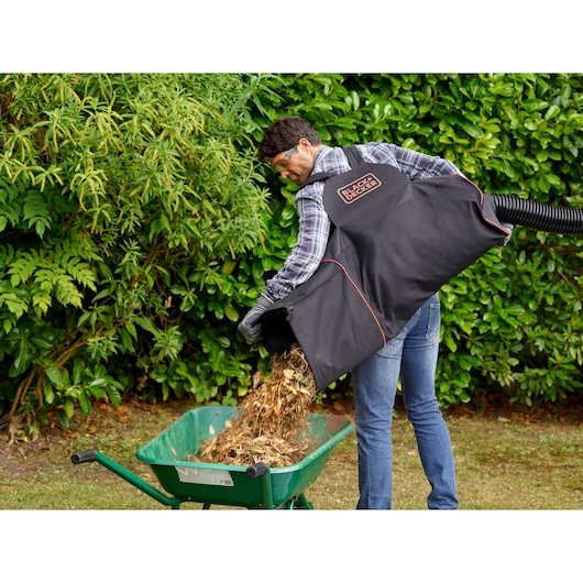 BLACKDECKER BEBLV300 tuinzuigzak in gebruik, mulch wordt in een groene kruiwagen buiten geleegd.