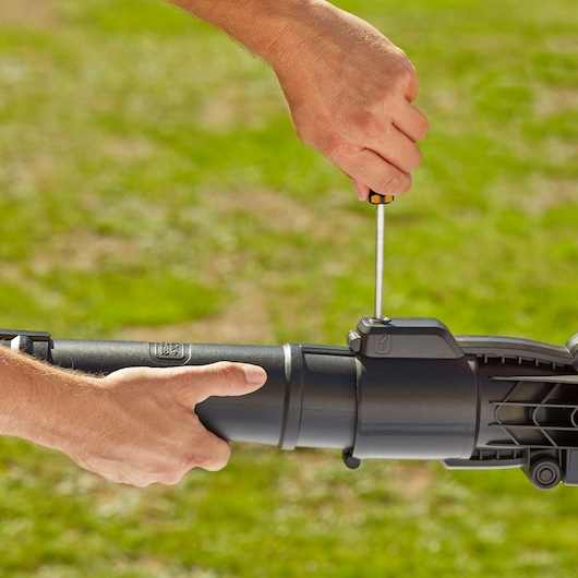 Foto van handen die de BLACKDECKER BEBLV300 blazerbuis buitenshuis monteren met een schroevendraaier.