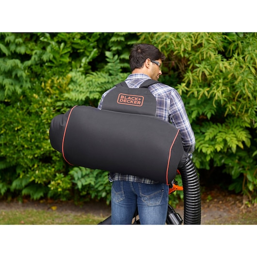 BLACKDECKER BEBLV301 bladzuigzak op de rug, zwart met oranje bies, tuin als achtergrond.