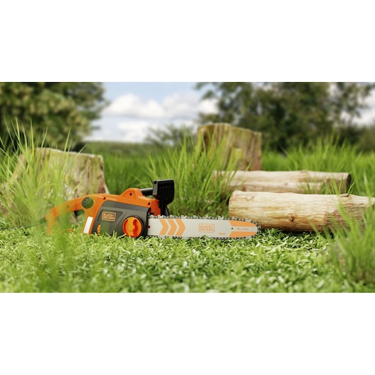 Foto van BLACK+DECKER BECS1835 kettingzaag op gras met boomstammen op de achtergrond, buiten.