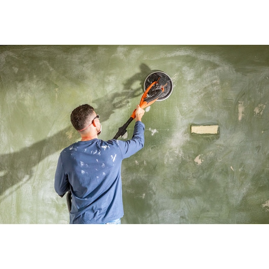 Persoon gebruikt een BLACK+DECKER wandenschuurmachine op een groene muur.