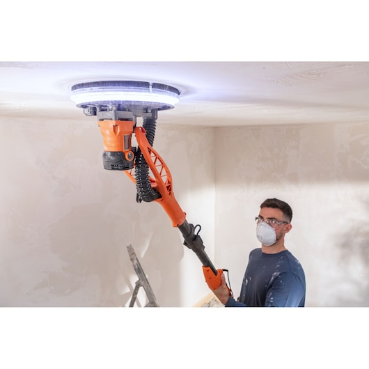 Persoon gebruikt BLACK+DECKER gipsplafondschuurmachine met LED-verlichting bij renovatie.