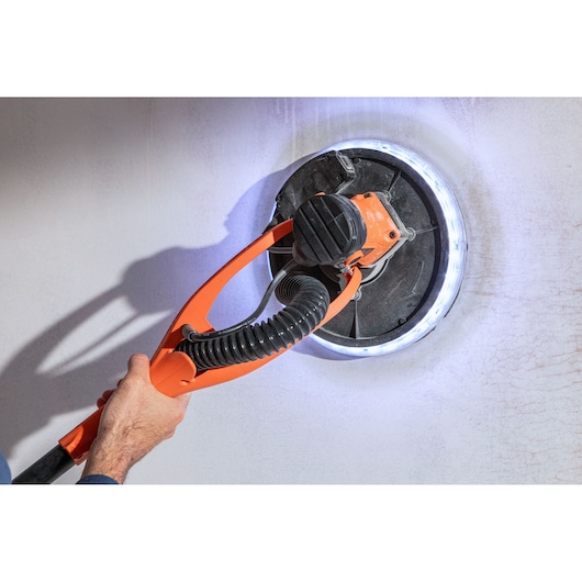 Iemand gebruikt een BLACK+DECKER muurschuurmachine met LED-licht voor het gladmaken van een muur.