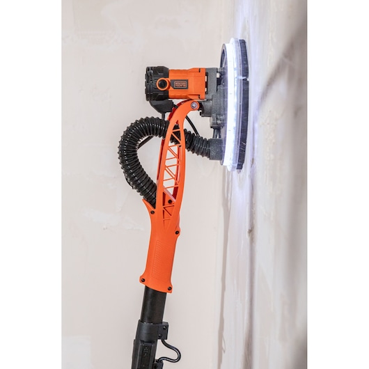 BLACK+DECKER muurschuurmachine met slang, schuurt een muur. Oranje en zwart handvat.