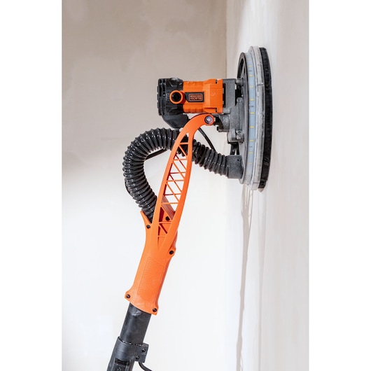 BLACK+DECKER muurschuurmachine met slang werkt op een witte muur.