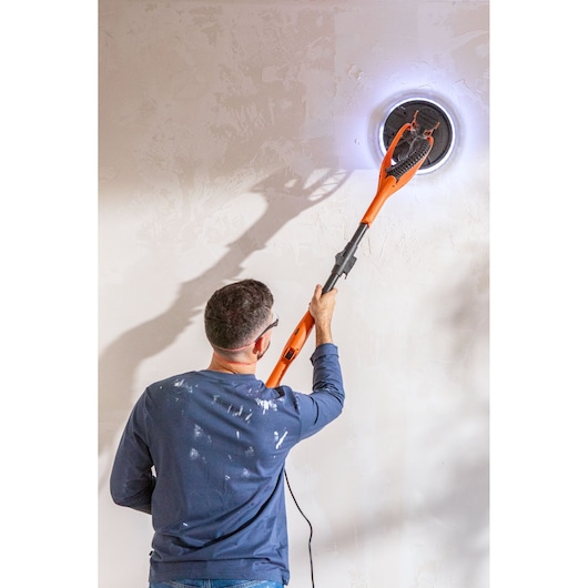 Persoon schuurt muur met BLACK+DECKER elektrische wandschuurmachine, LED-ring rond schuurkop.