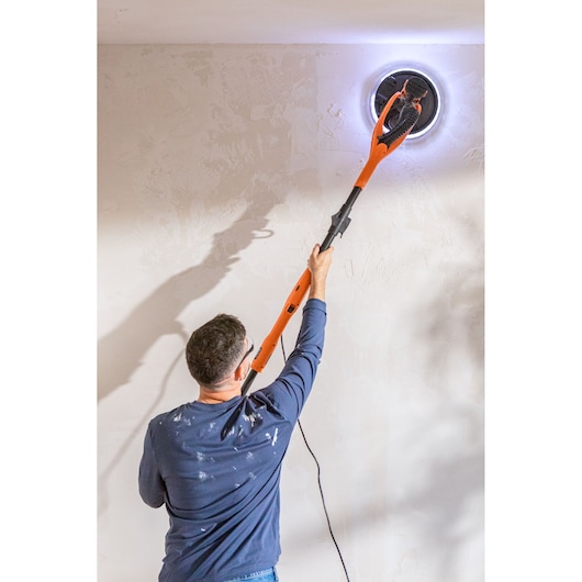 Persoon schuurt plafond met BLACK+DECKER LED-gypswand schuurmachine.