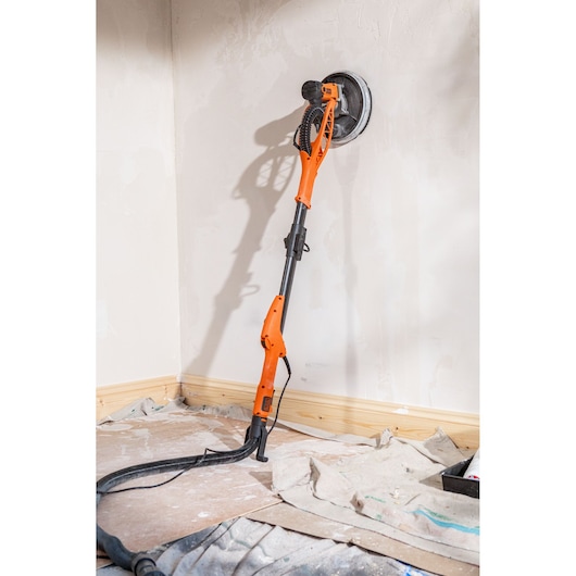 Oranje BLACKDECKER gipswand schuurmachine tegen een muur in een kamer in renovatie, slang aan de basis aangesloten.