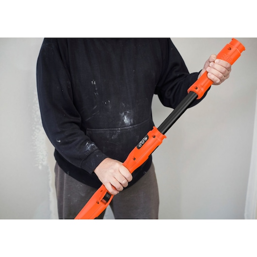 Persoon houdt BLACKDECKER BEDW700A8S gipsmuurschuurmachine met oranje behuizing en zwart handvat vast.