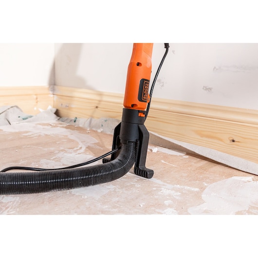 BLACK+DECKER schuurmachine met stofslang, schuurt nabij een muur op een bouwvloer.