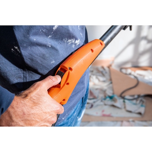Hand houdt een oranje handgreep van een BLACK+DECKER gereedschap vast met trekkerknop in werkruimte.