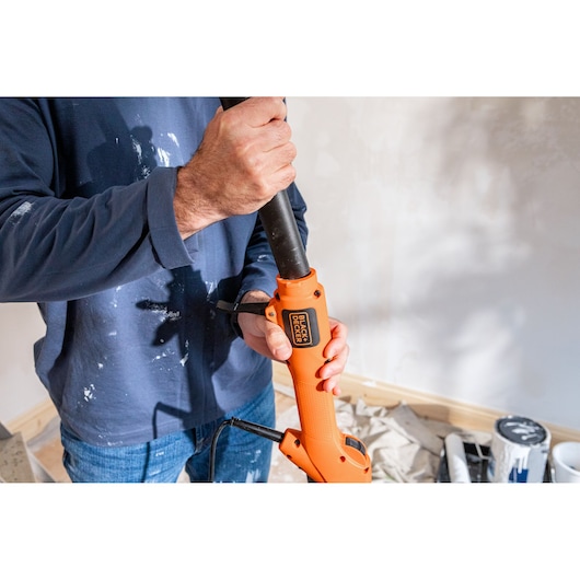 Persoon houdt een oranje BLACK+DECKER elektrisch gereedschap vast in een kamer met schilderbenodigdheden.